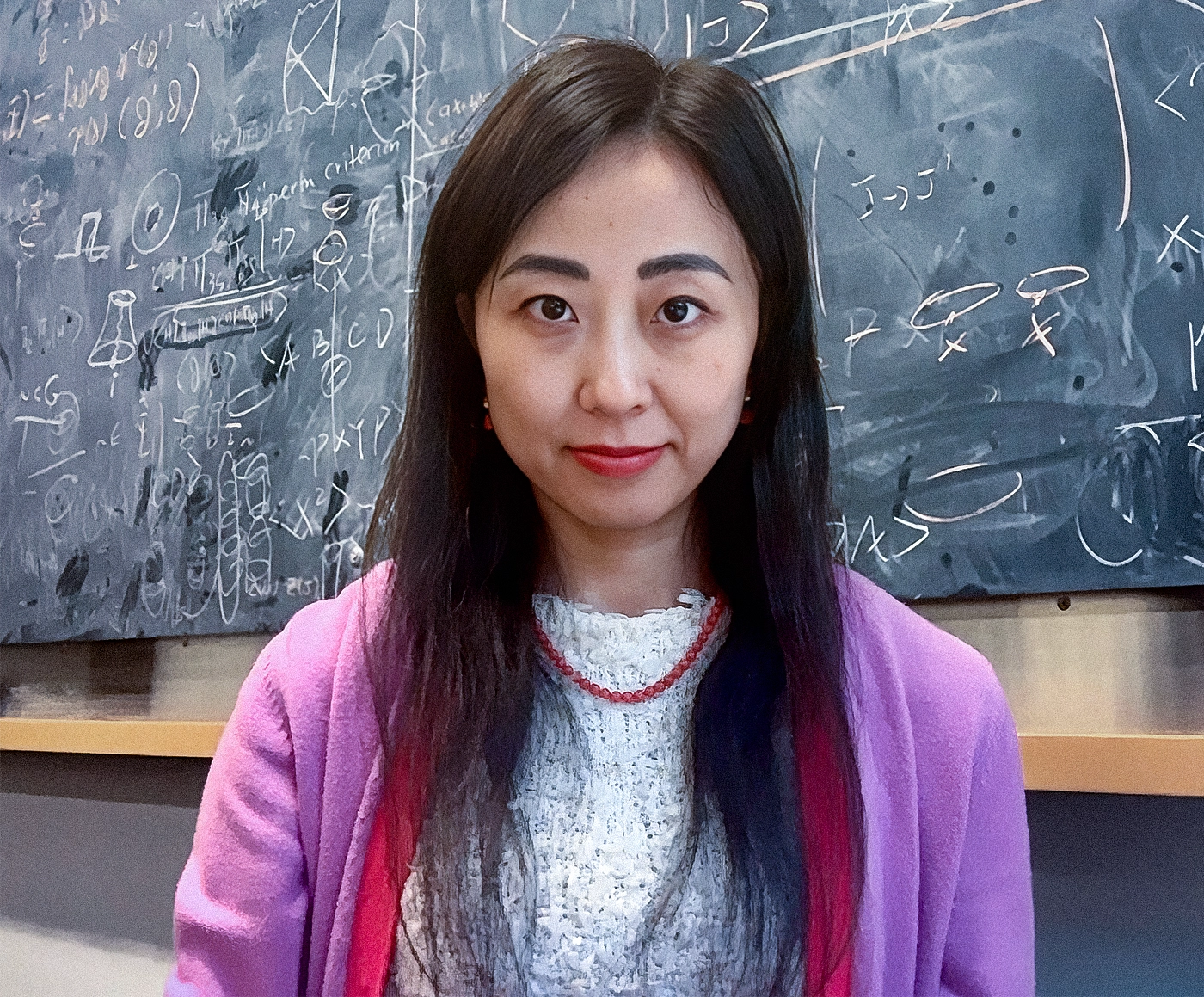 A woman in a pink sweater in front of a chalk board.