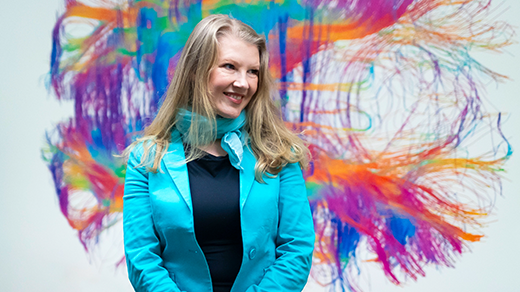 Ev Fedorenko smiles in front of a rainbow mural of a brain.