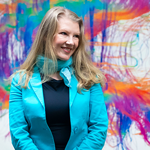 Ev Fedorenko smiles in front of a rainbow mural of a brain.