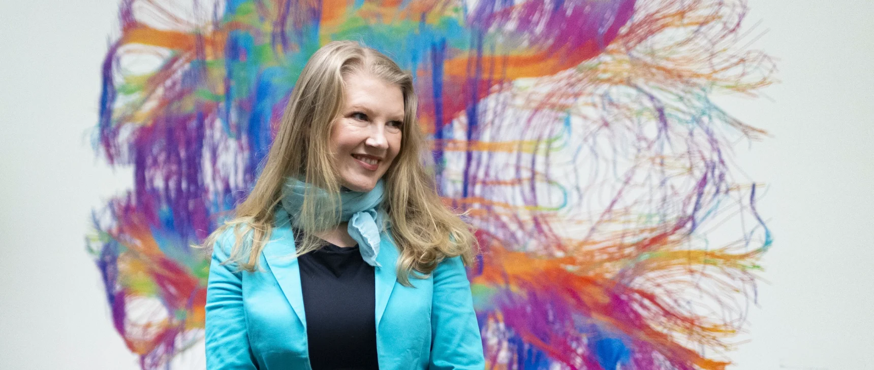 Ev Fedorenko smiles in front of a rainbow mural of a brain.