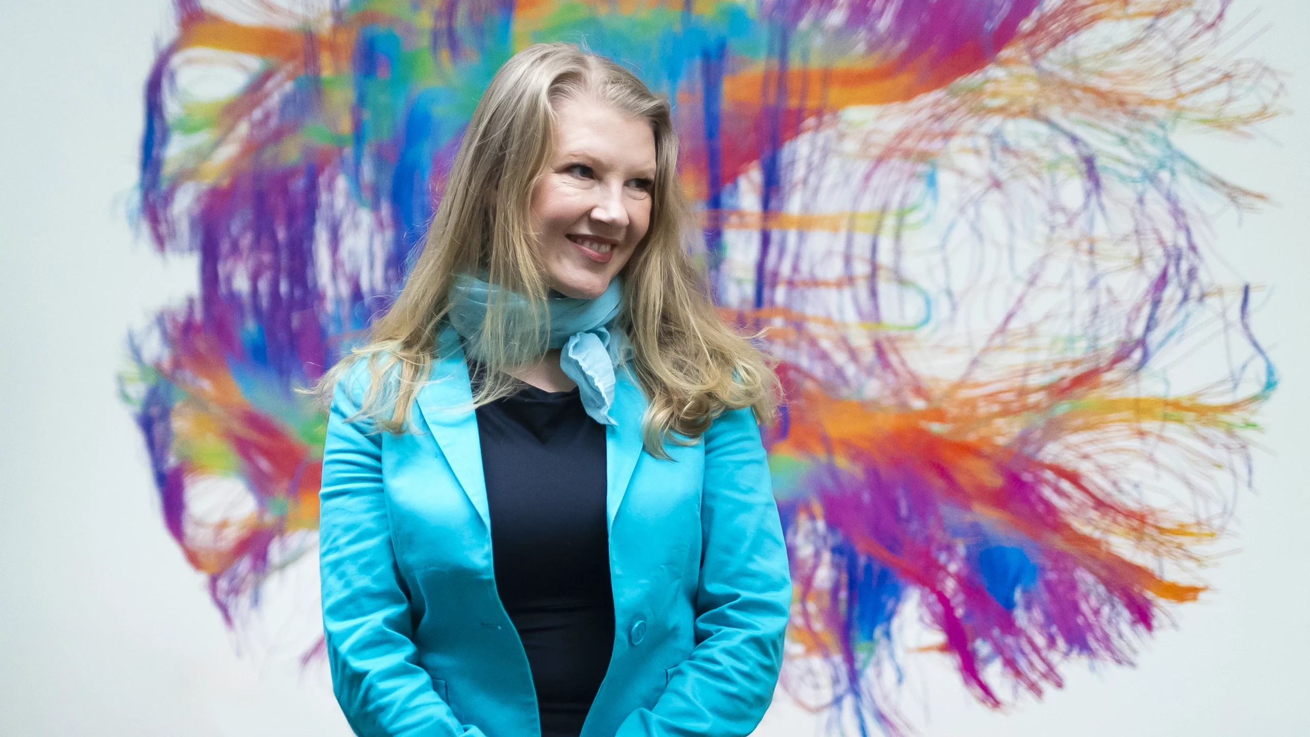 Ev Fedorenko smiles in front of a rainbow mural of a brain.