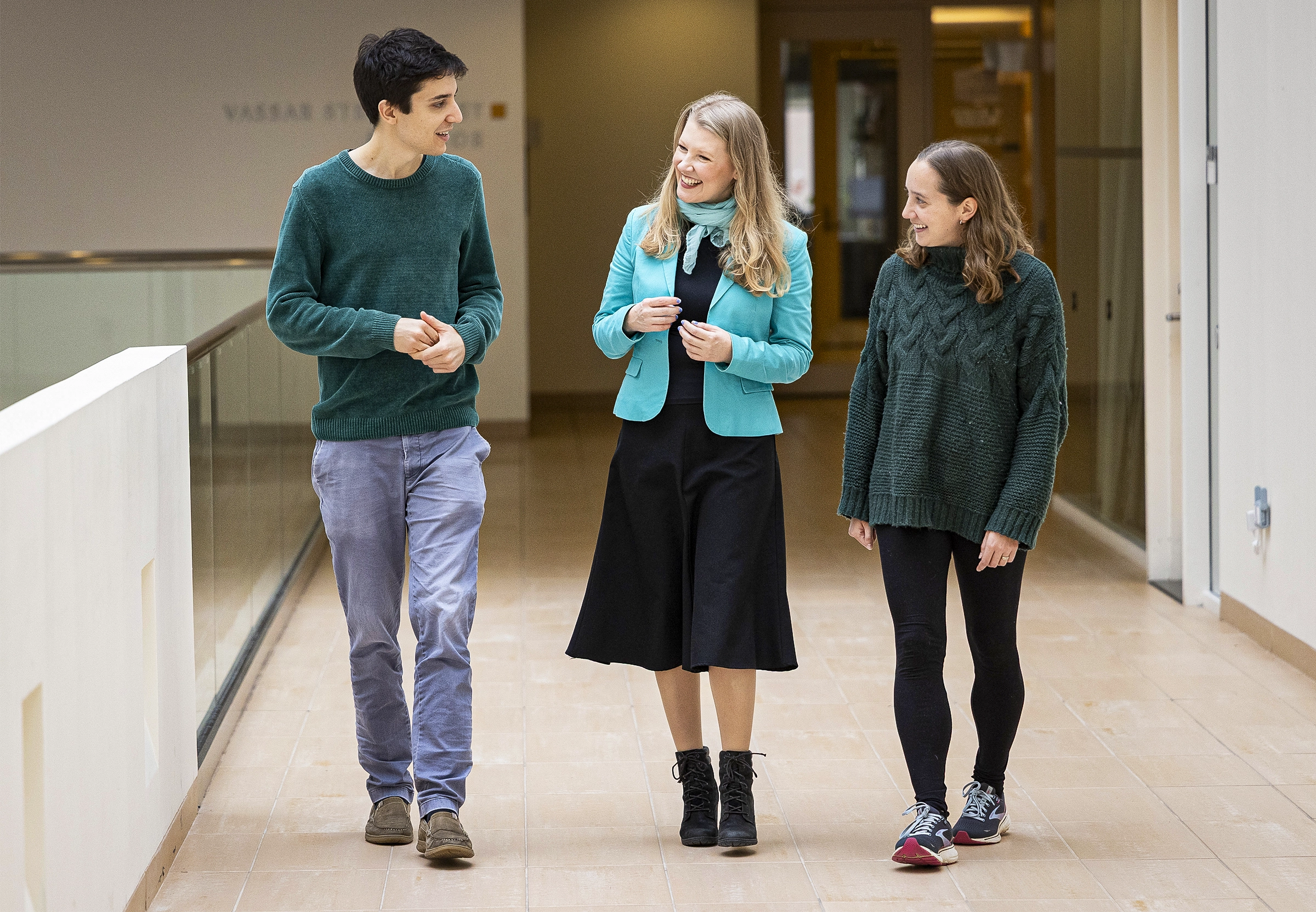 Three people walk down a hallway toward the camera.