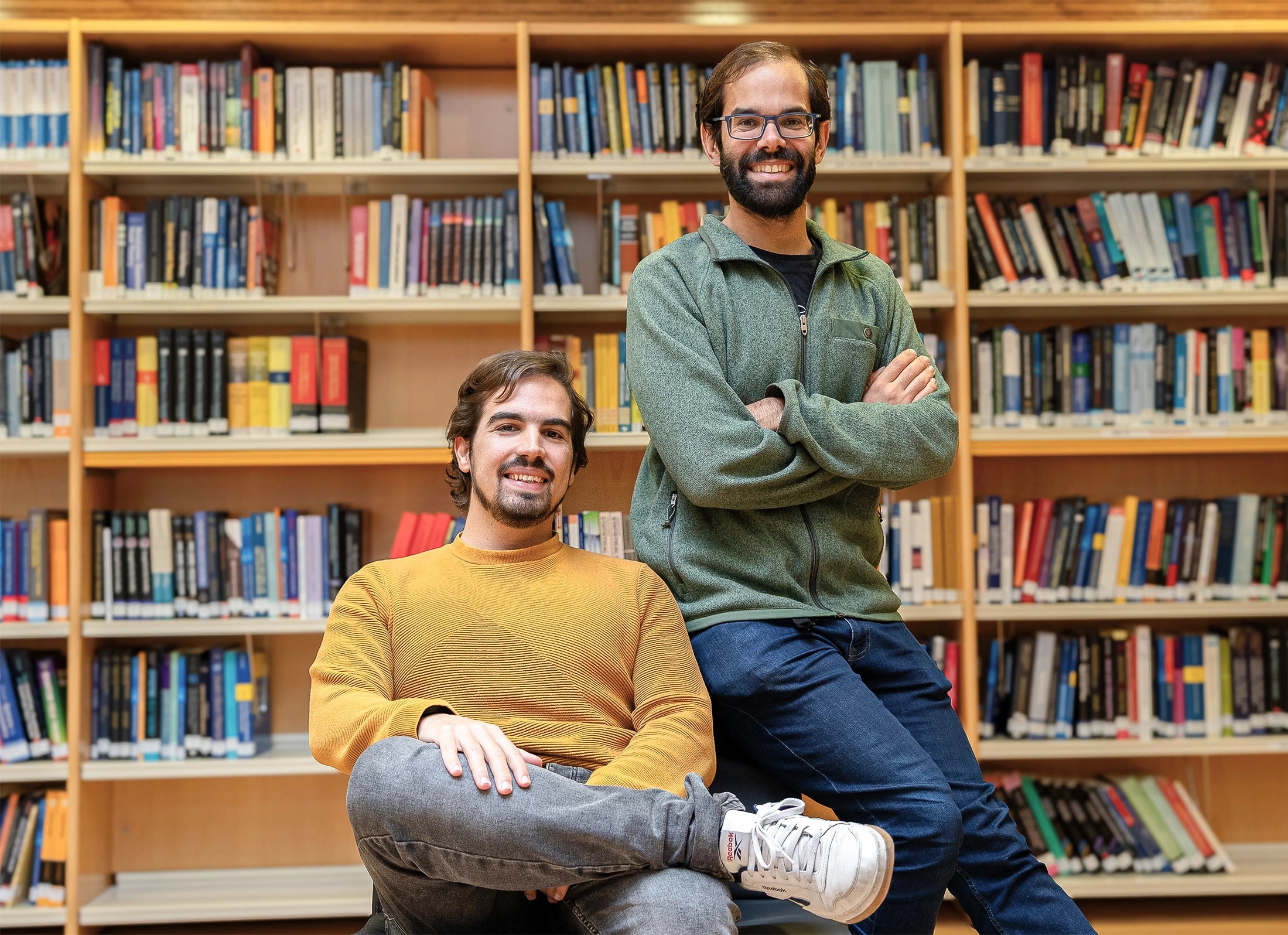 Two men smile at the camera in a library