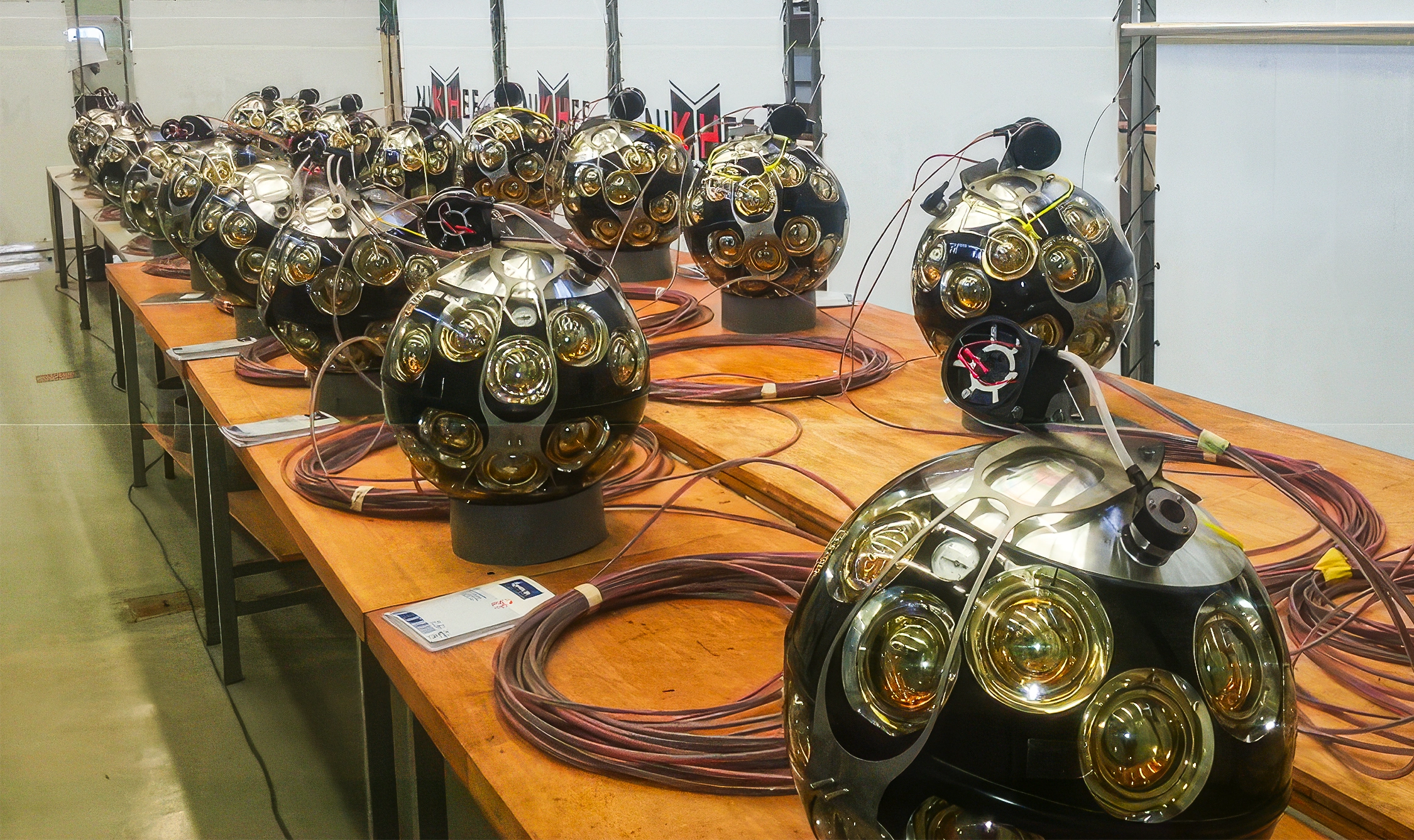 More than a dozen roughly basketball-sized spherical detectors, connected with coils of dark red cable, are staged in two lines on top of a long row of tables pushed together.