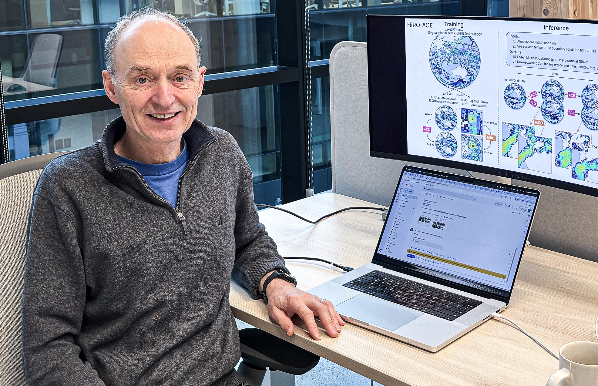 A man wearing a sweater sits at a workstation.