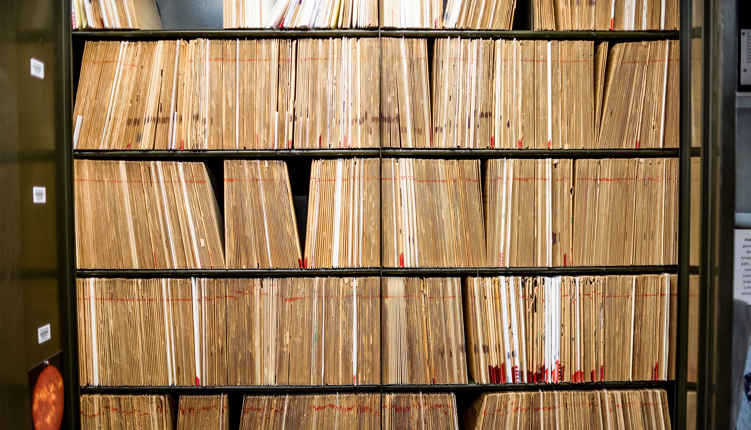 A set of shelves vertically hold hundreds of paper-covered glass photographic plates.