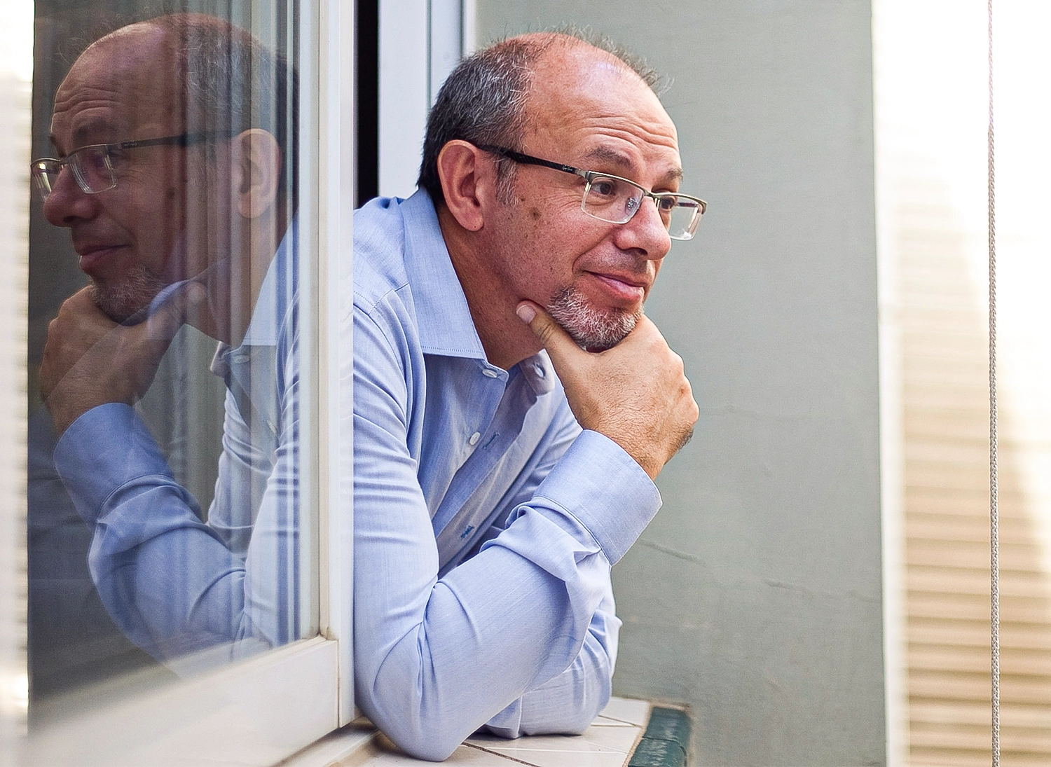 Man in glasses leaning out of a window.