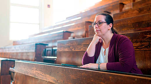 A woman in a purple sweater sits at a bench in a lecture hall.