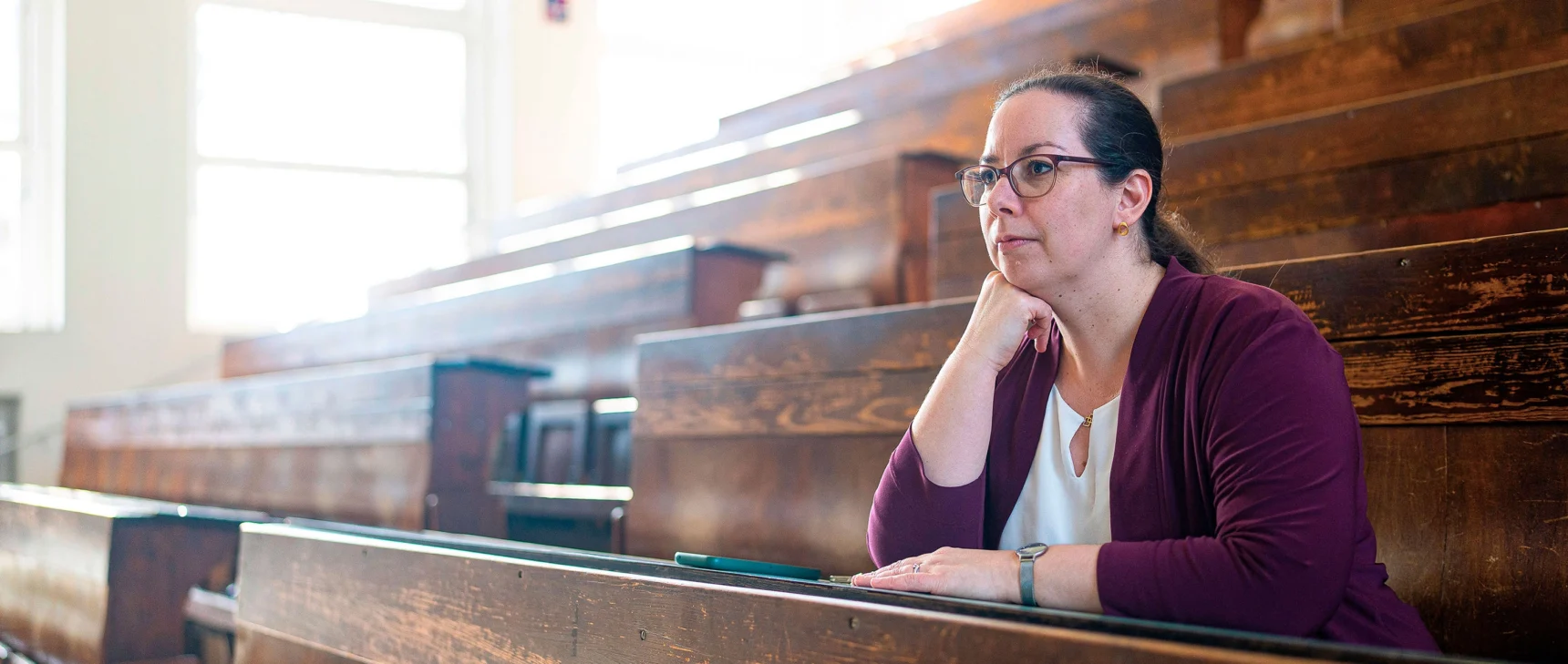 A woman in a purple sweater sits at a bench in a lecture hall.