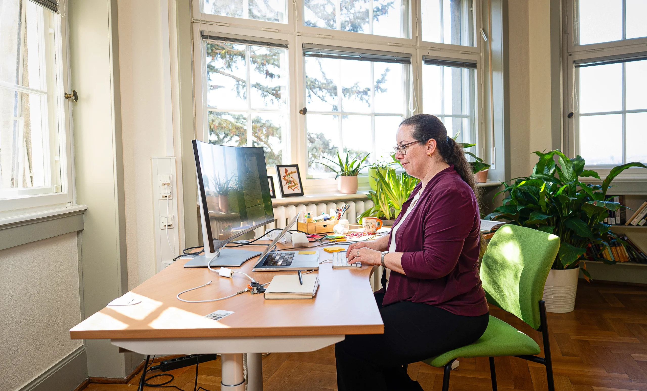 A woman sits at a computer in a sun-drenched office.