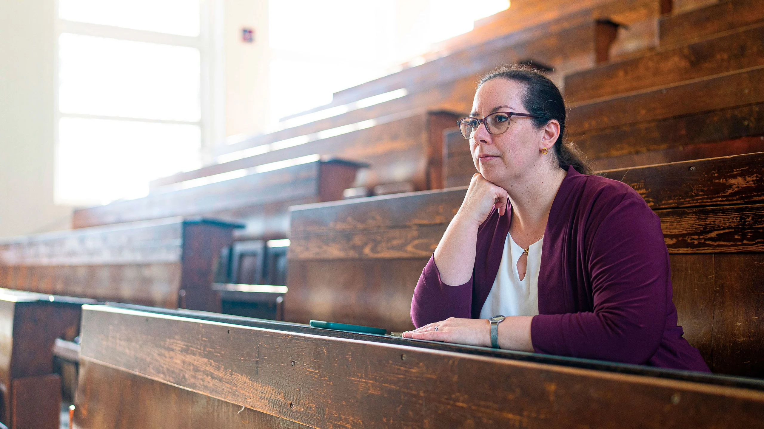 A woman in a purple sweater sits at a bench in a lecture hall.
