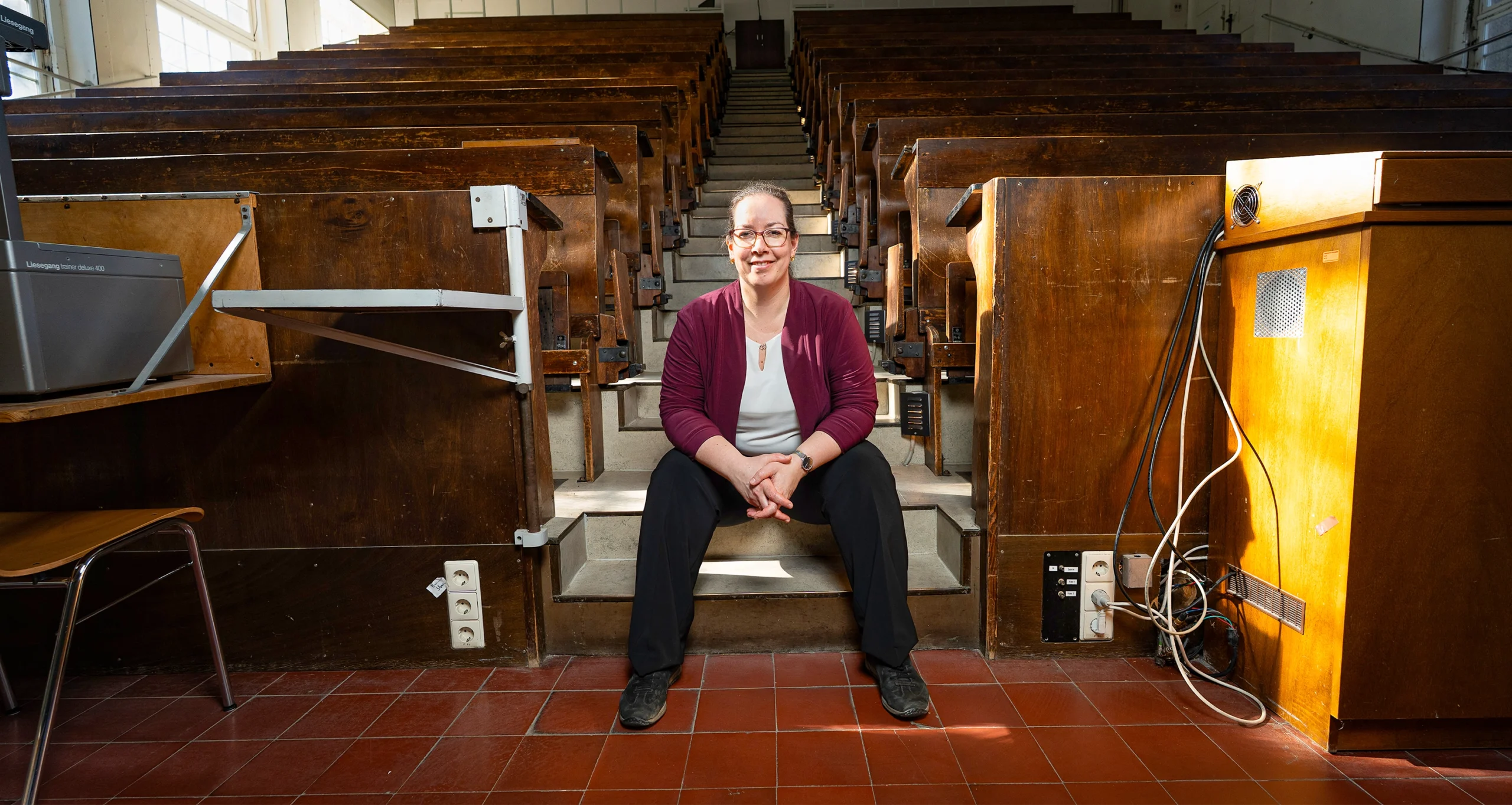 A woman sits in the middle of a lecture hall, with rows of benches receding behind her.