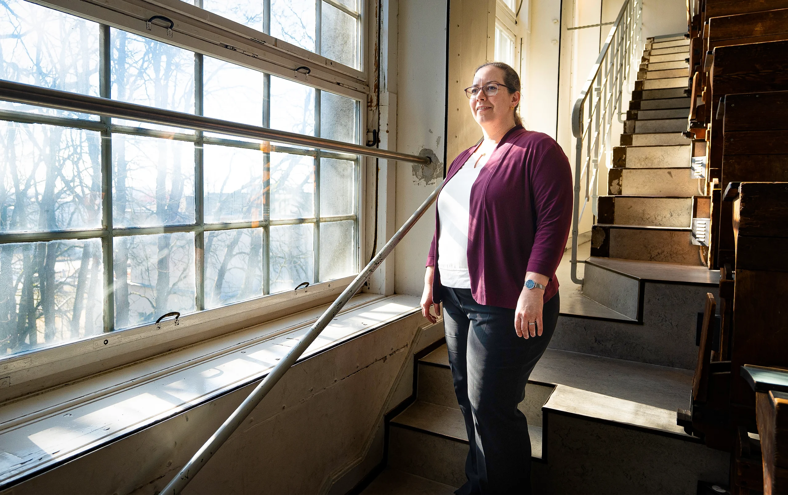 A woman stands by a window on a staircase.
