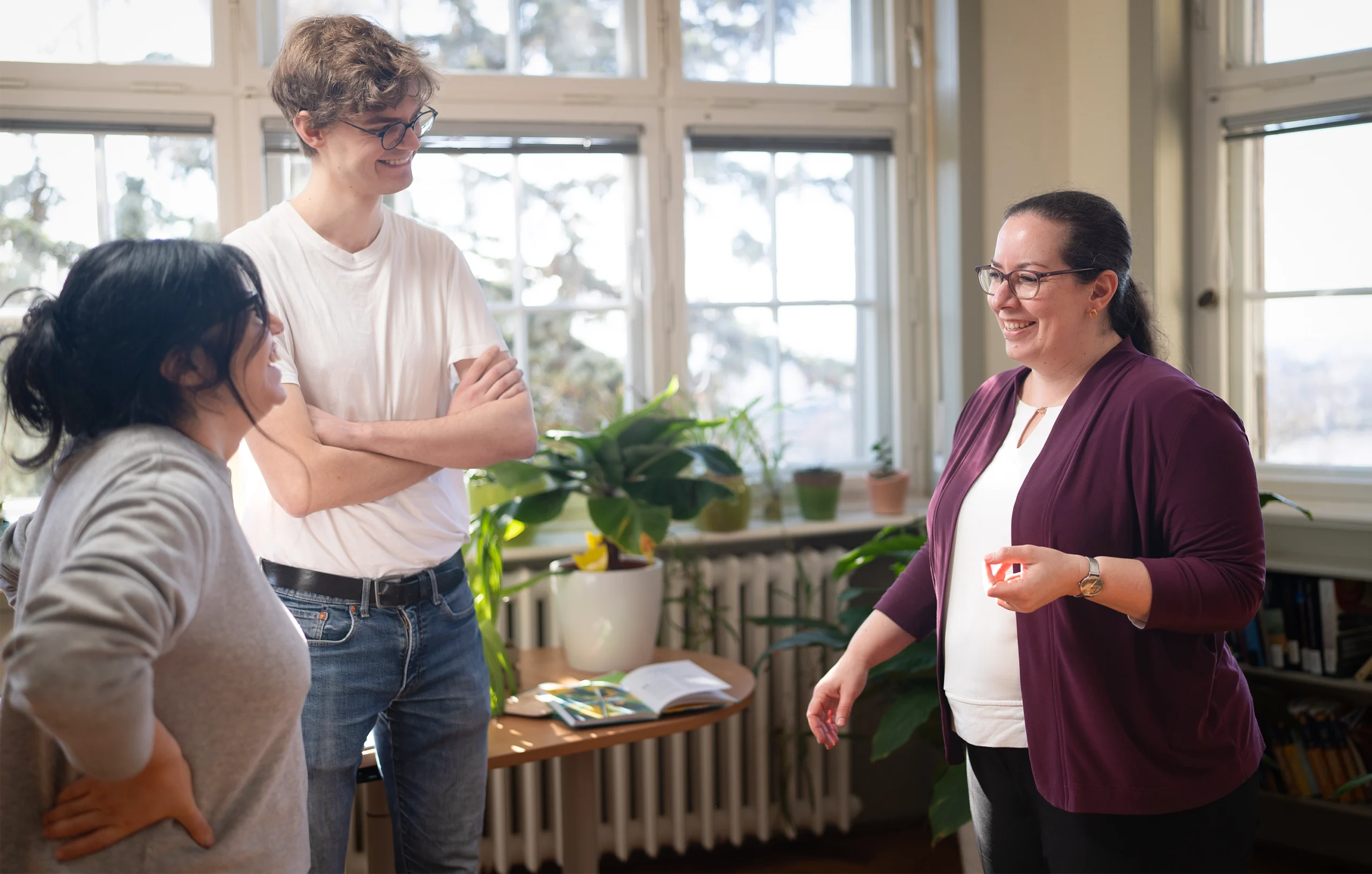 A woman stands in a sunny office, having a discussion with two young collaborators.