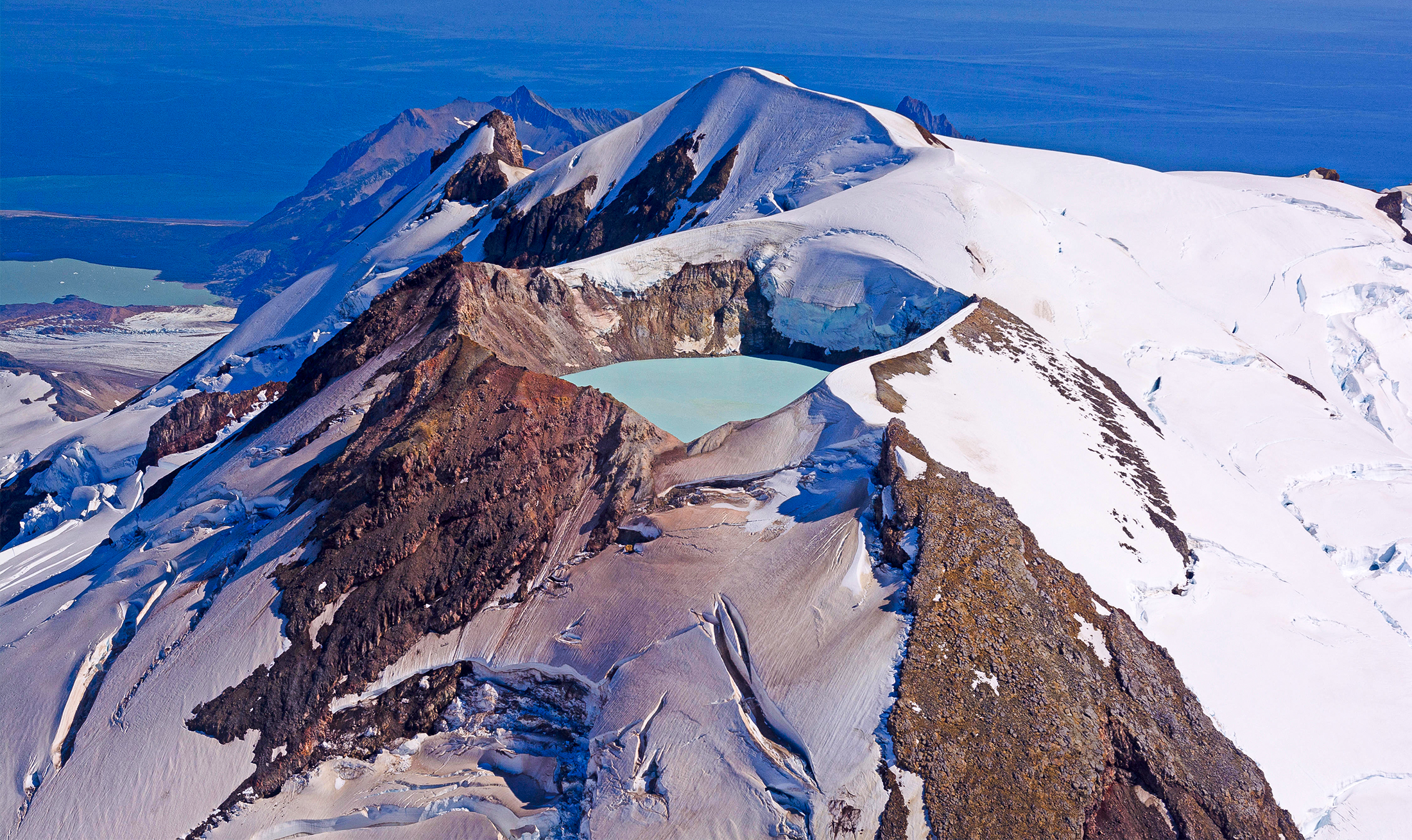 The peak of a snow-covered mountain has been replaced with a deep crater filled with water.