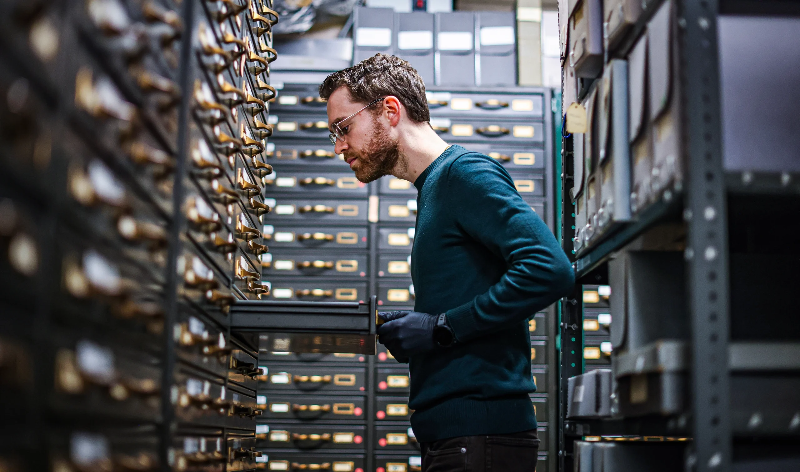 Man in a museum archive, looking into a drawer.