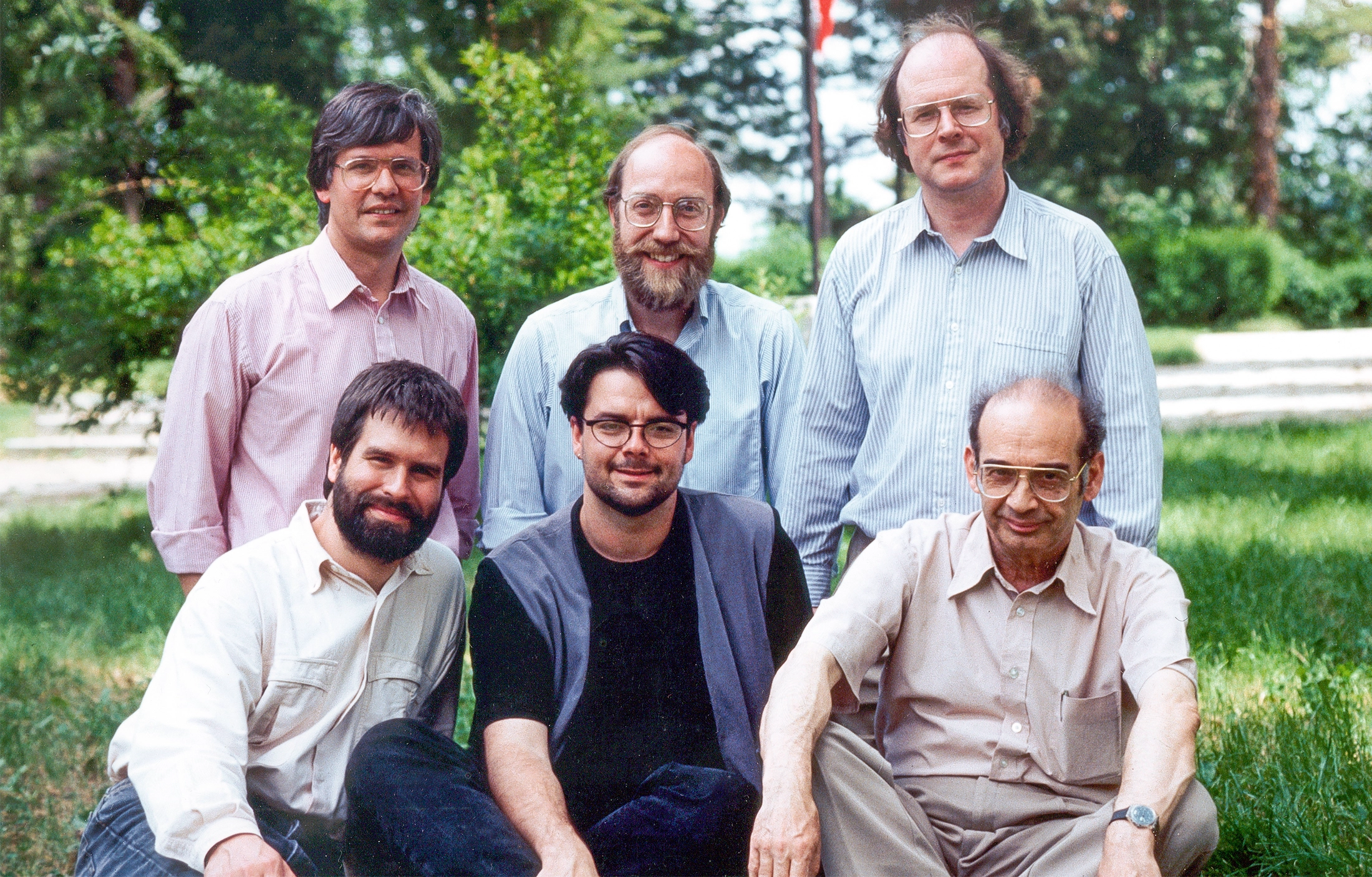 Six men posing for a photo on a grassy field.