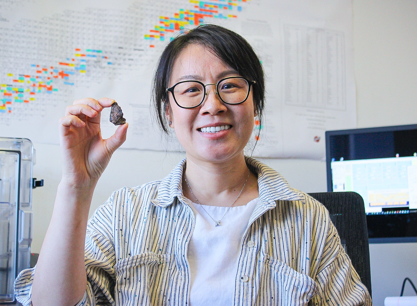 A woman holds up what looks like a small rock with her index finger and thumb.