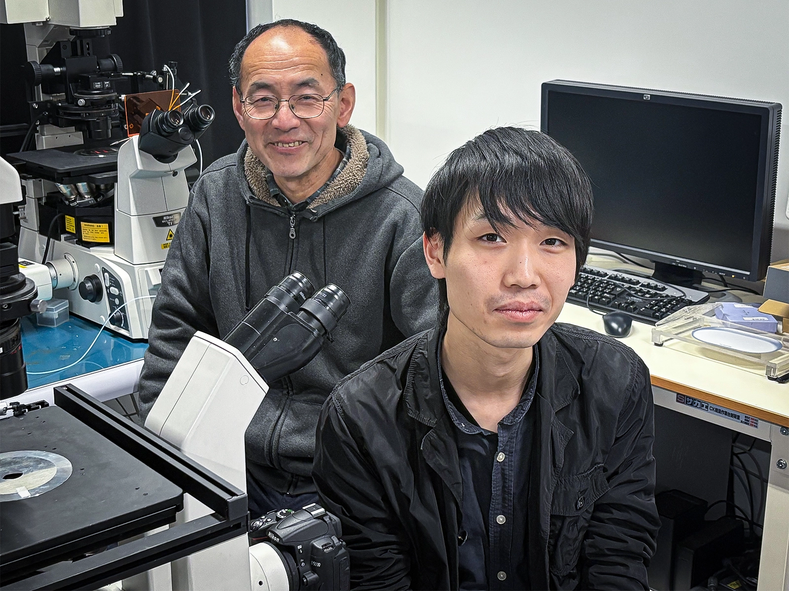 Ryusaku Deguchi and Ruka Kitsui sit next to a microscope.