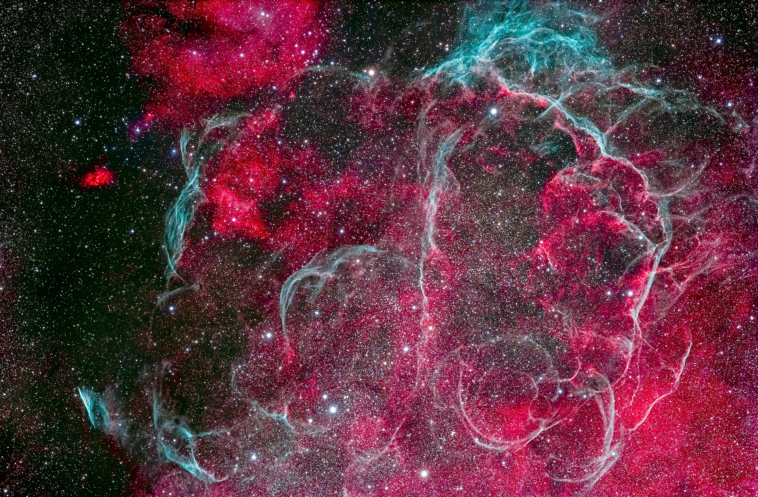 An image in space shows billowing clouds of red and light blue against a background of stars.