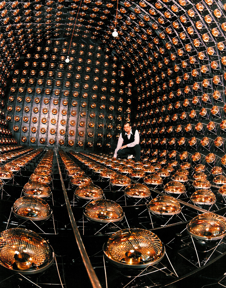 A man crouches inside a black, cylindrical space studded with reflective, semispherical detectors.