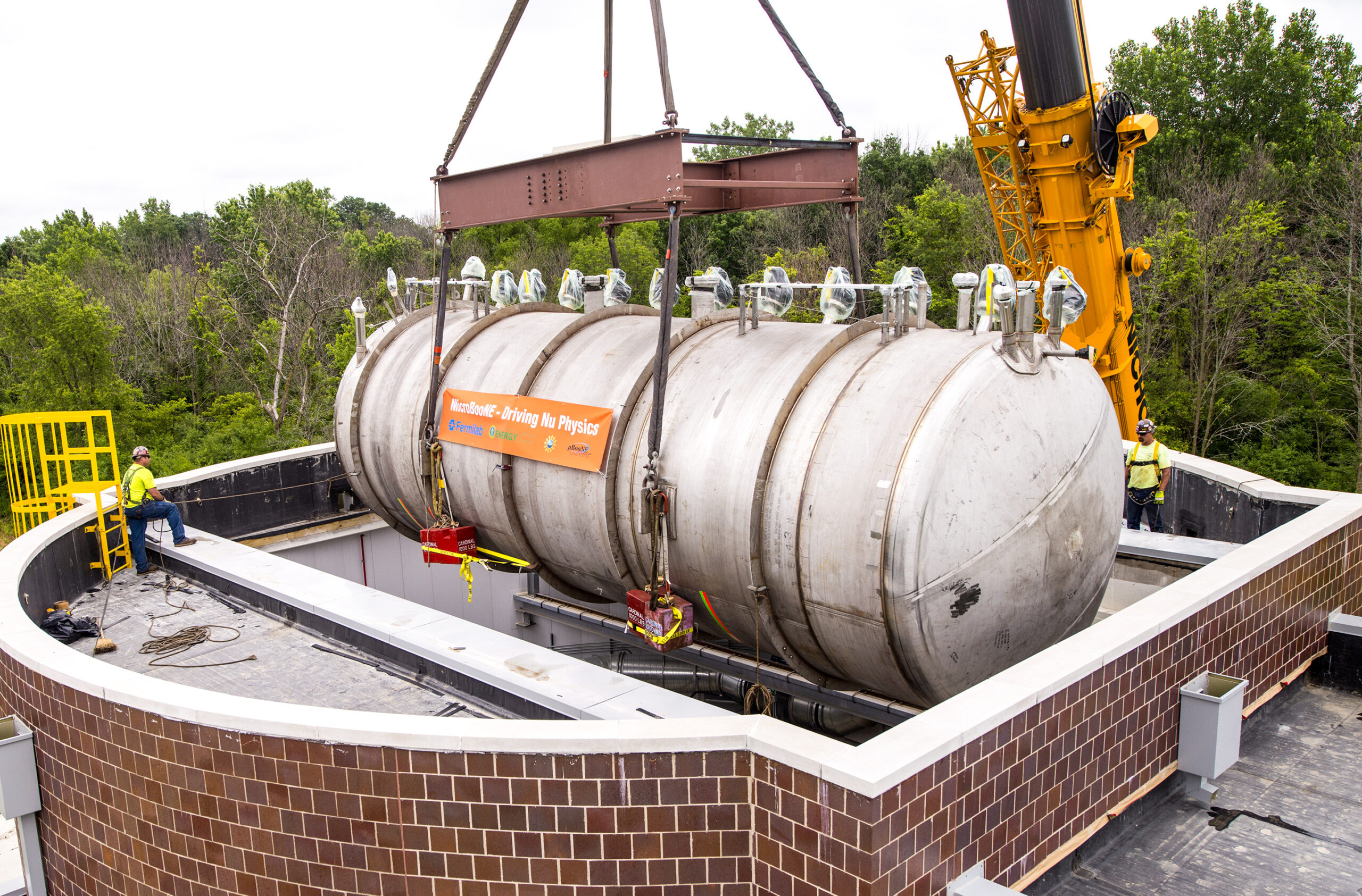 A crane lowers a metallic cylinder into a round brick building.