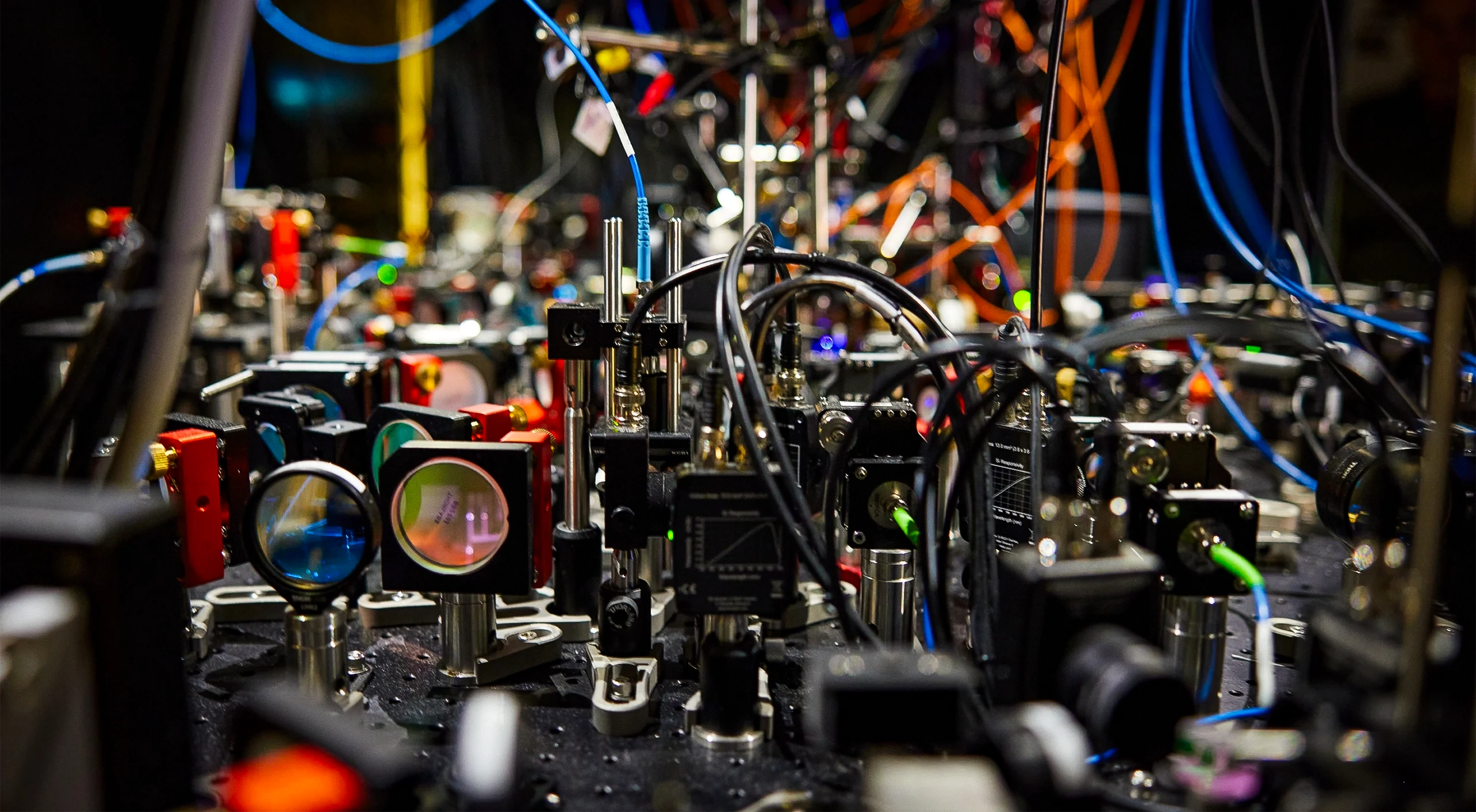 A tangle of cables connects devices on an optical table in a lab.
