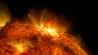 Video showing a slow-moving edge of the red-colored sun pointing upwards. A large solar flare erupts, starting at the right and moving towards the center as the edge of the sun rotates anti-clockwise.