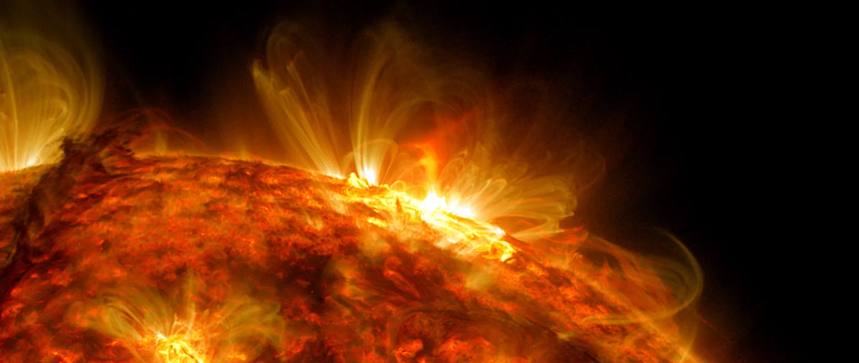Video showing a slow-moving edge of the red-colored sun pointing upwards. A large solar flare erupts, starting at the right and moving towards the center as the edge of the sun rotates anti-clockwise.