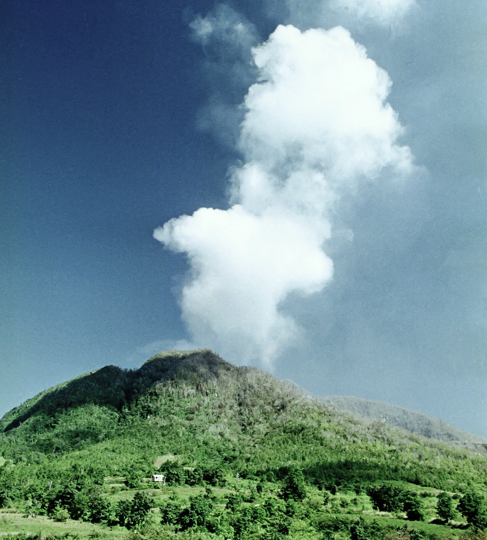 A green mountain with smoke billowing out of the top