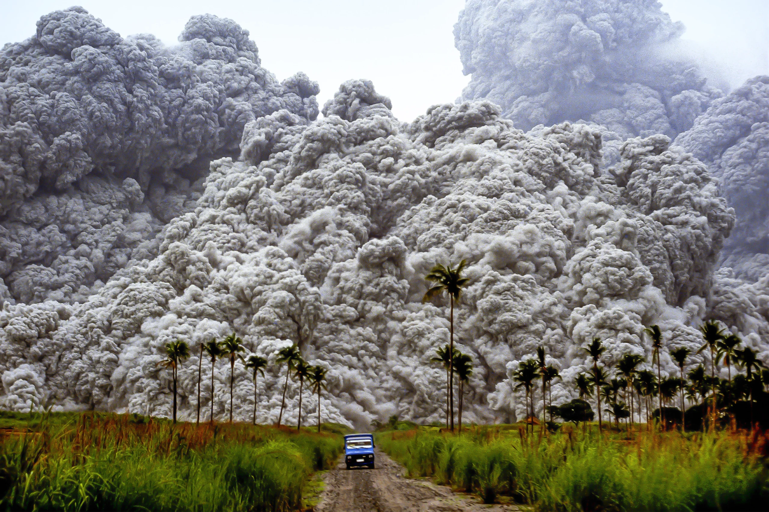 A lone car driving away from a huge volcanic erupty