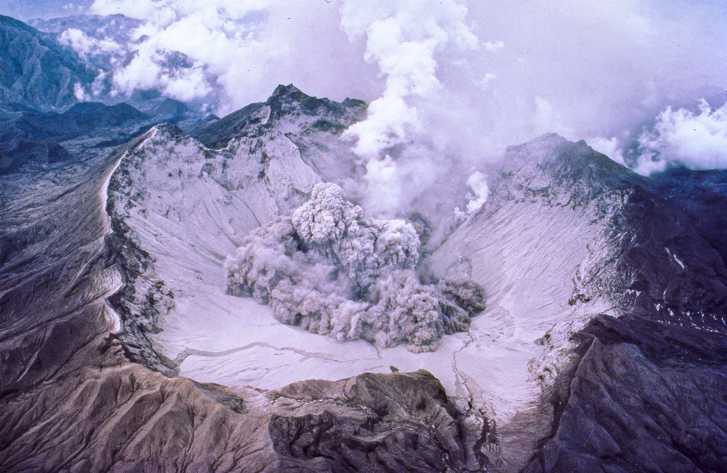 A crater at the top of a volcano with smoke billowing out