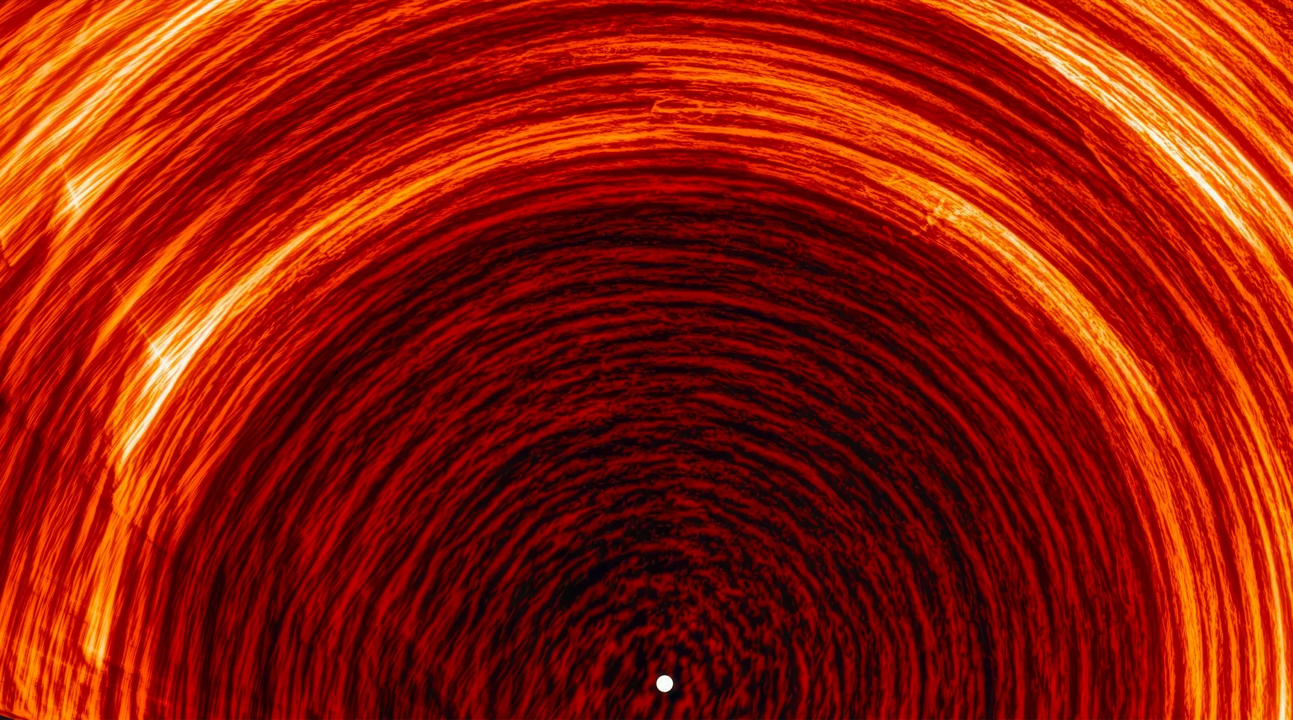 A visualization in deep red, orange, and white of the sun’s magnetic field in motion. Hundreds of tightly packed, semi-circular field lines form a dome around a single small white point at the bottom center.
