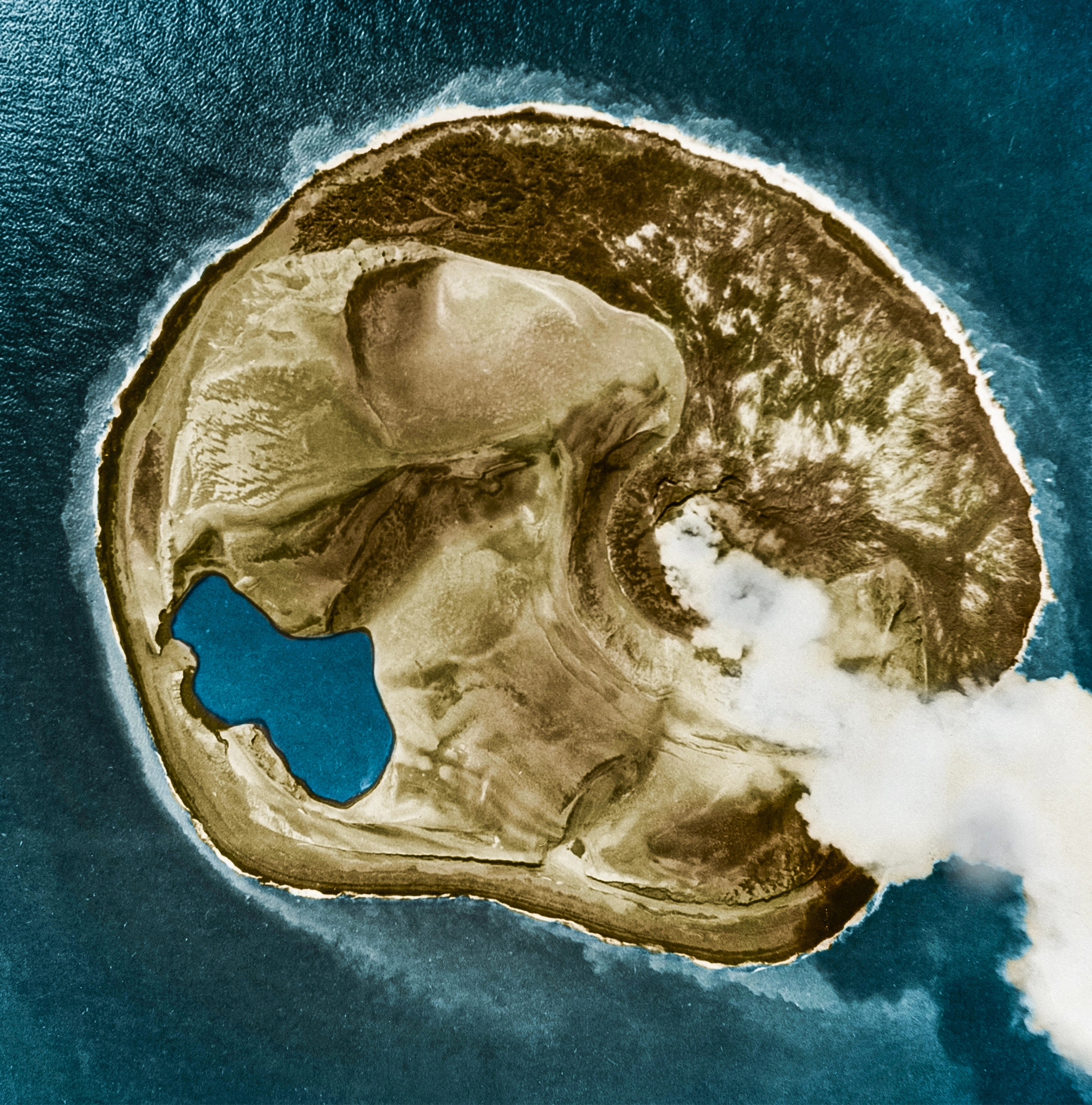 An aerial view shows a round island releasing a plume of white smoke.