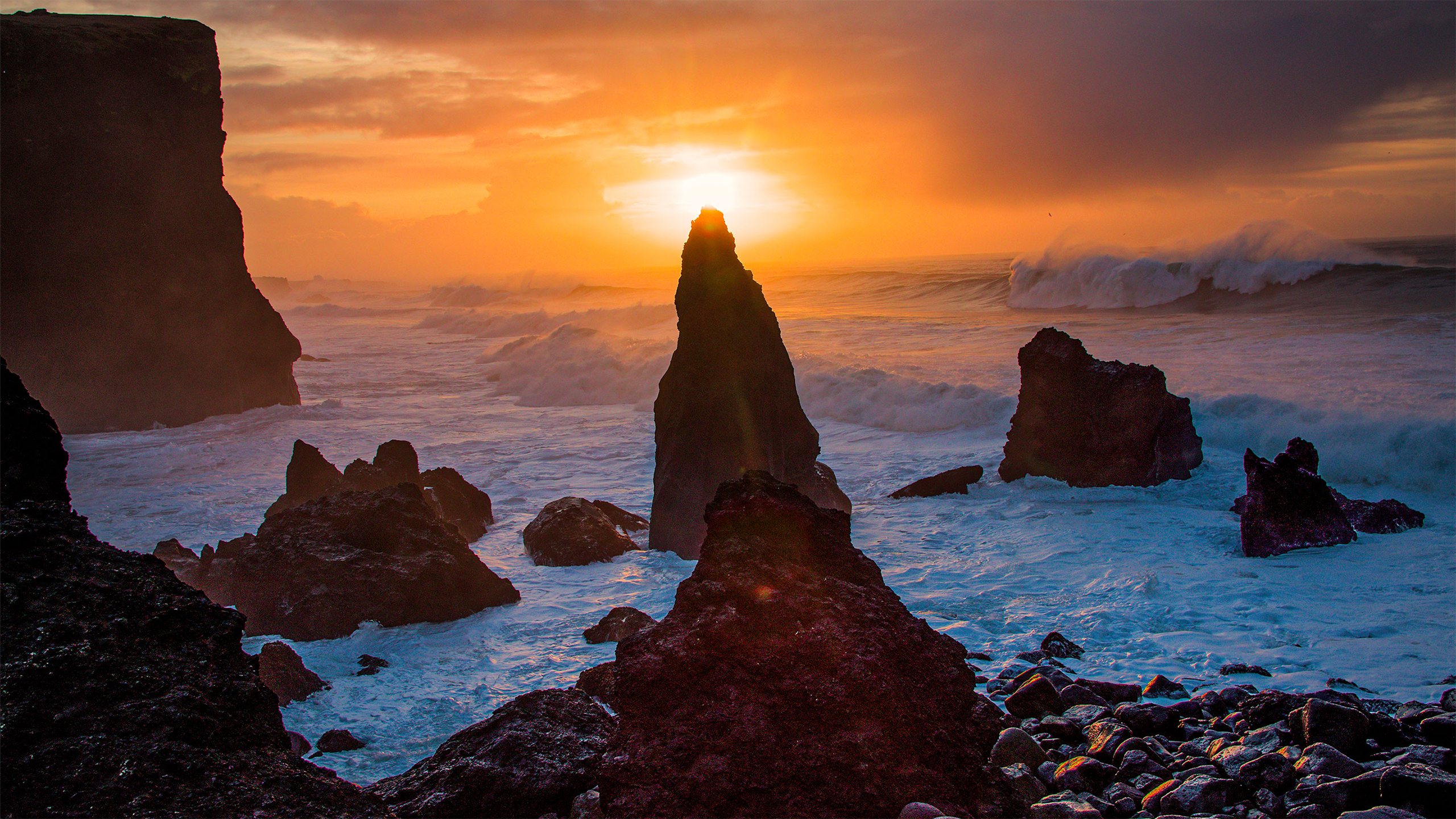 Rock formations emerge from the waves along the shore of Iceland.