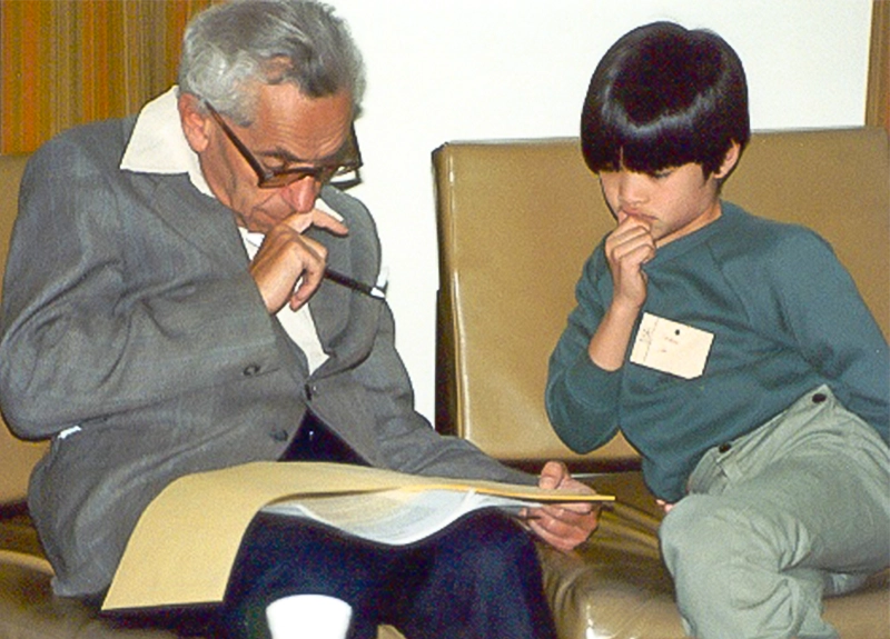 An old man and a young boy sitting together, both contemplating the same piece of paper