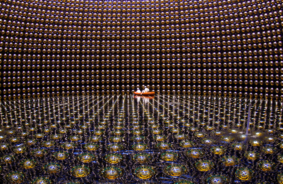 A large cavern lined with reflective spheres and partially filled with water. Two people in white protective gear float in an orange raft in the distance.