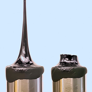 Video showing black, gooey liquids pulled apart in an extensional rheometer. In the first video, the liquid stretches. In the second video, the liquid cracks apart.