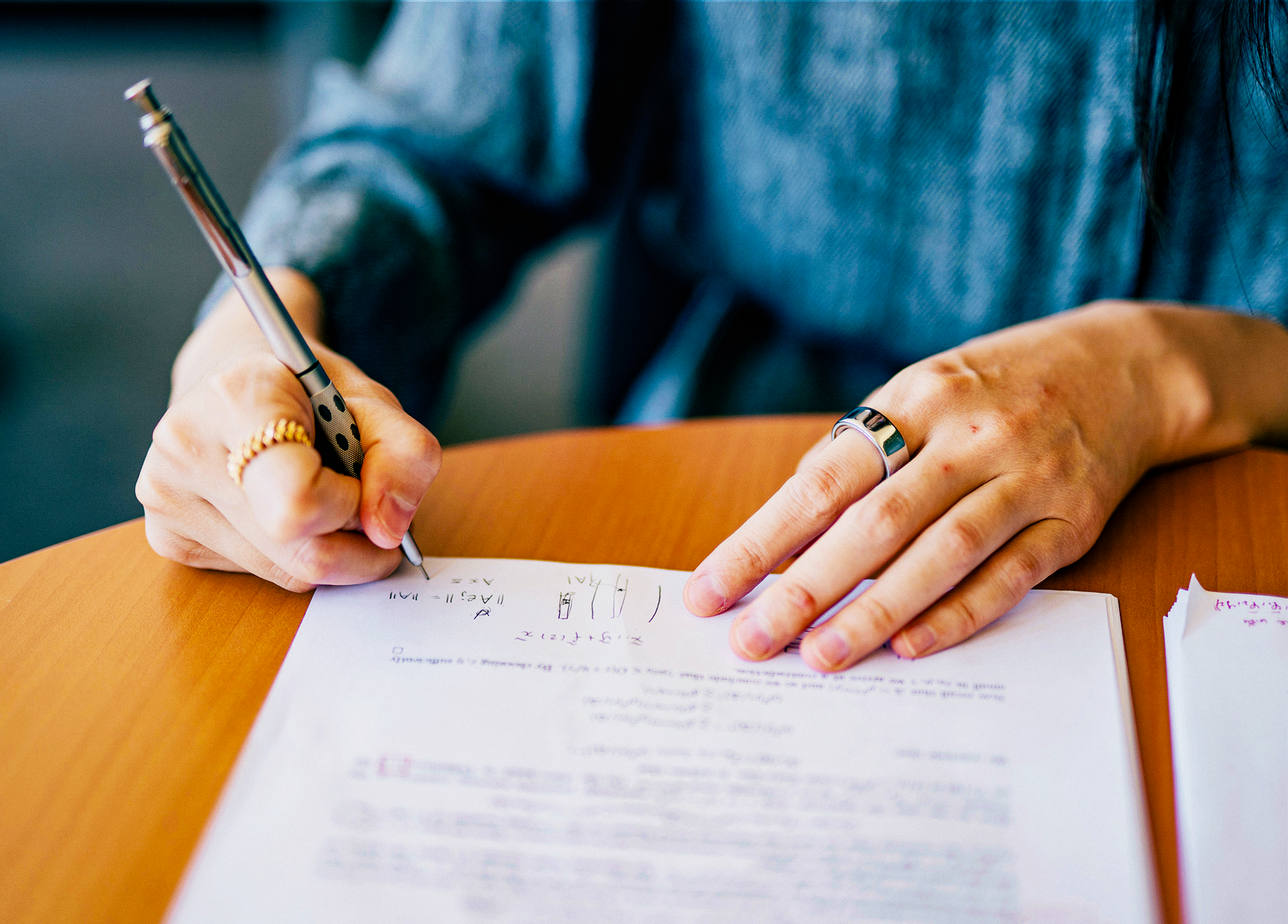 Two hands, with a ring on each index finger, writing mathematical notation.