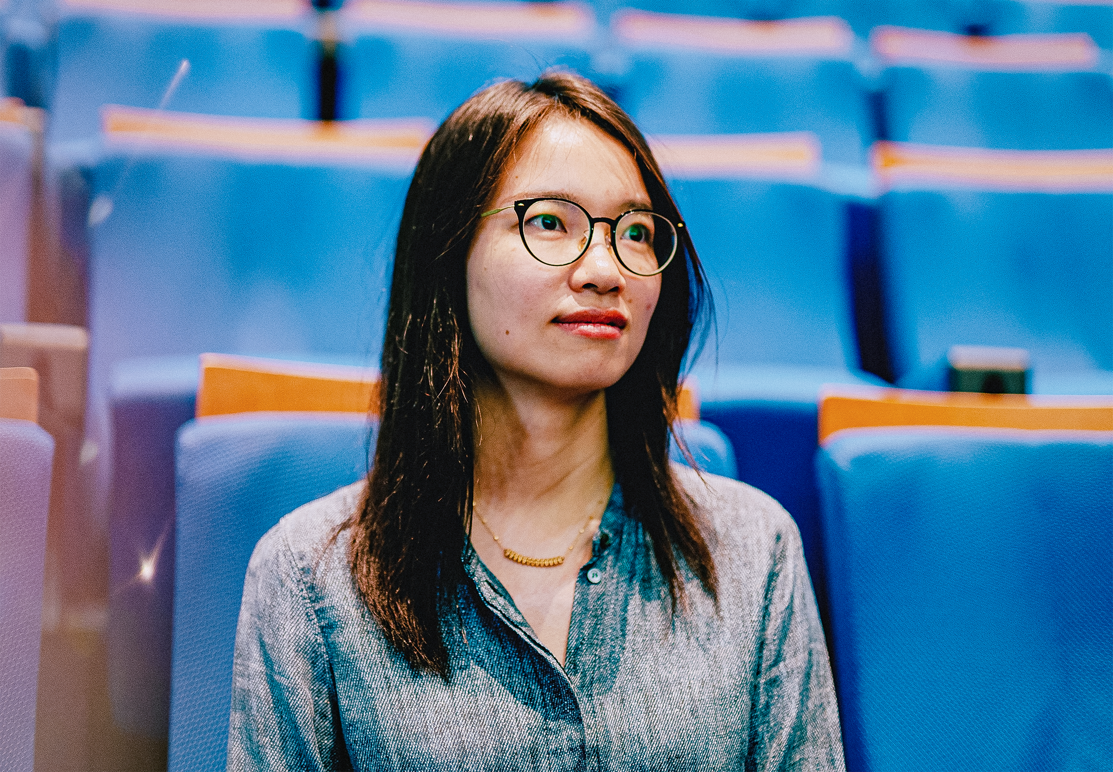 A closeup of a woman seated in an auditorium with blue seats.