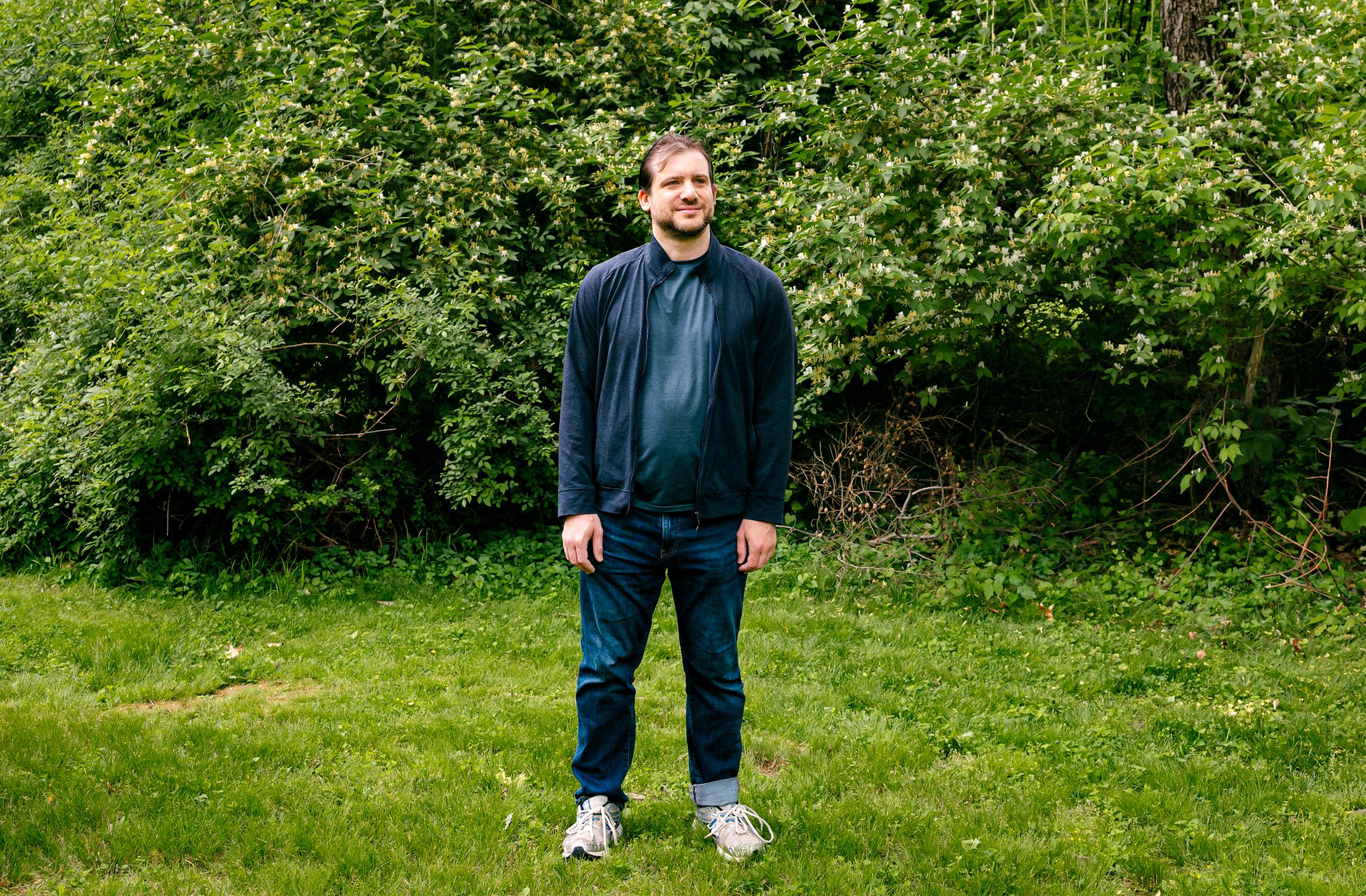 A man standing on grass in front of bushes.