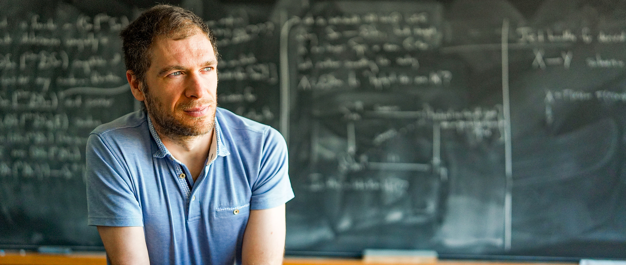 Man in a blue shirt in front of a blackboard.
