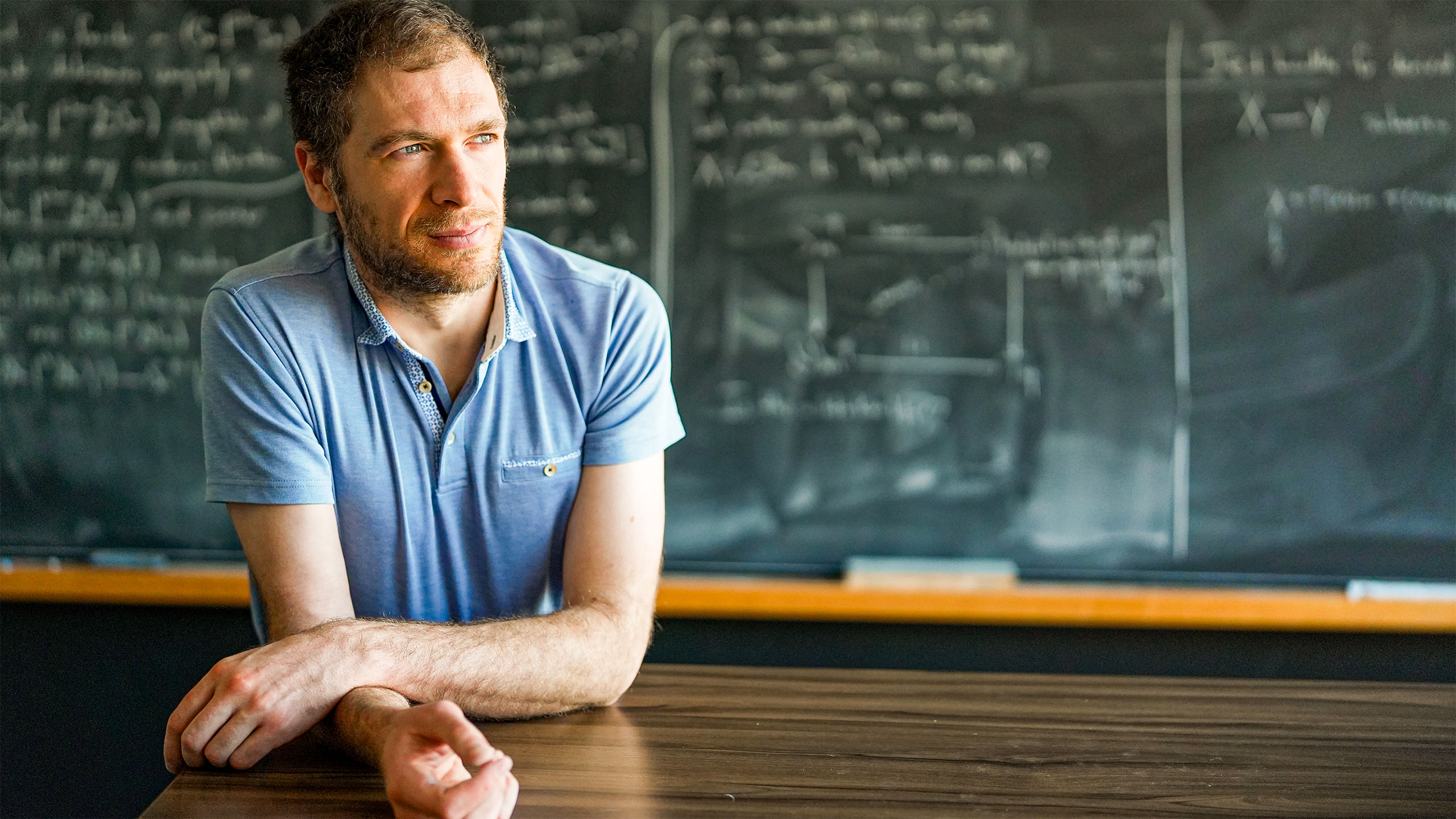 Man in a blue shirt in front of a blackboard.
