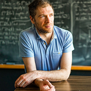 Man in a blue shirt in front of a blackboard.