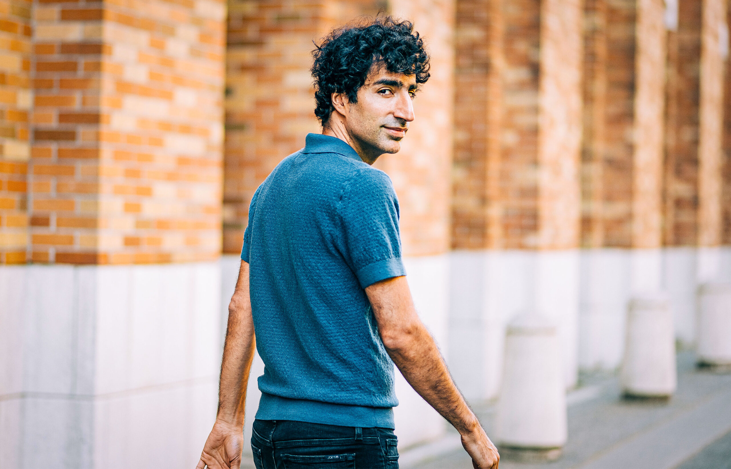 Shayan Oveis Gharan, wearing a navy polo shirt, walking away and turning back to look at the camera over his right shoulder.