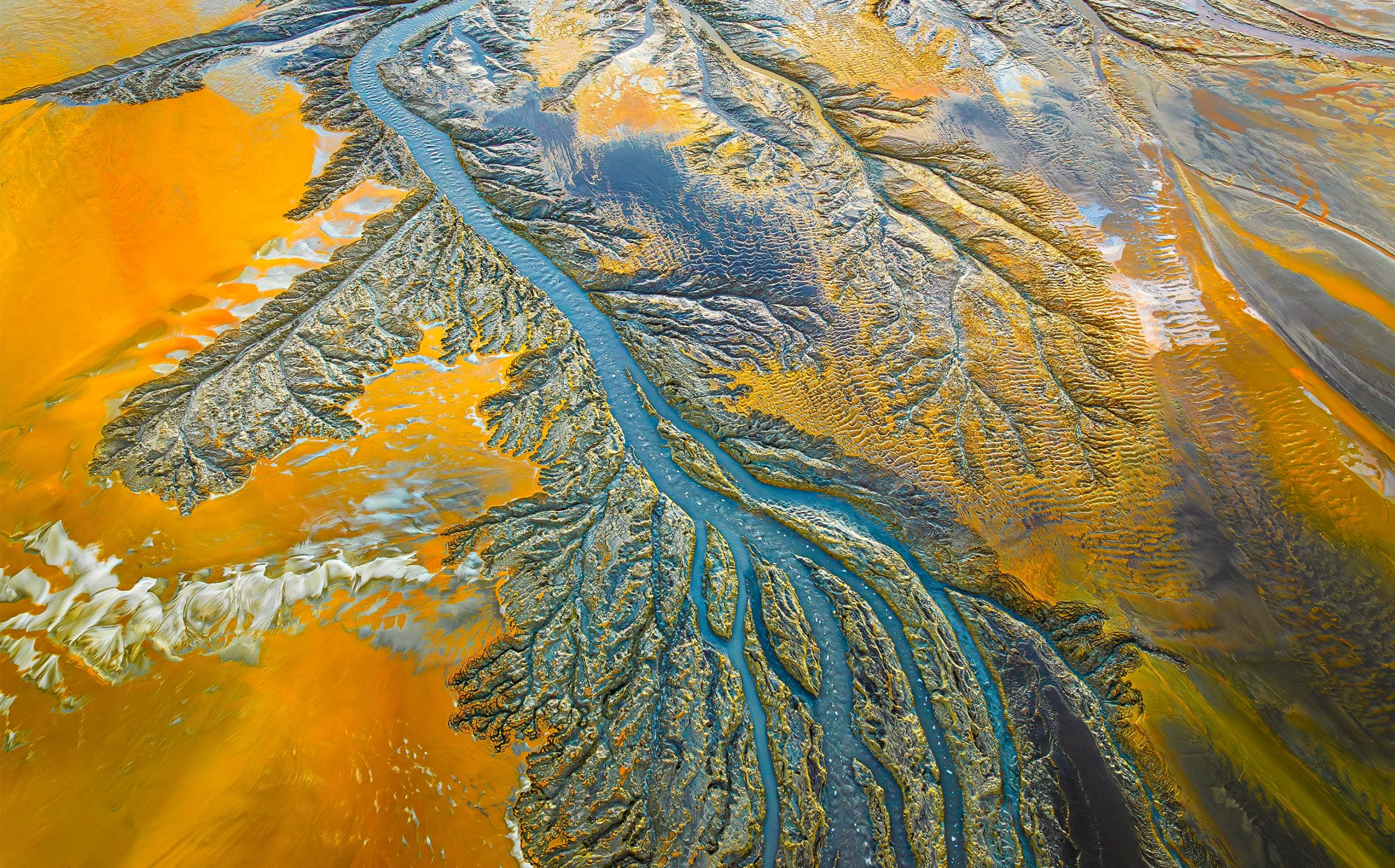 An aerial photo shows a braided river network cutting through a landscape, in Spain, stained orange by mining waste.