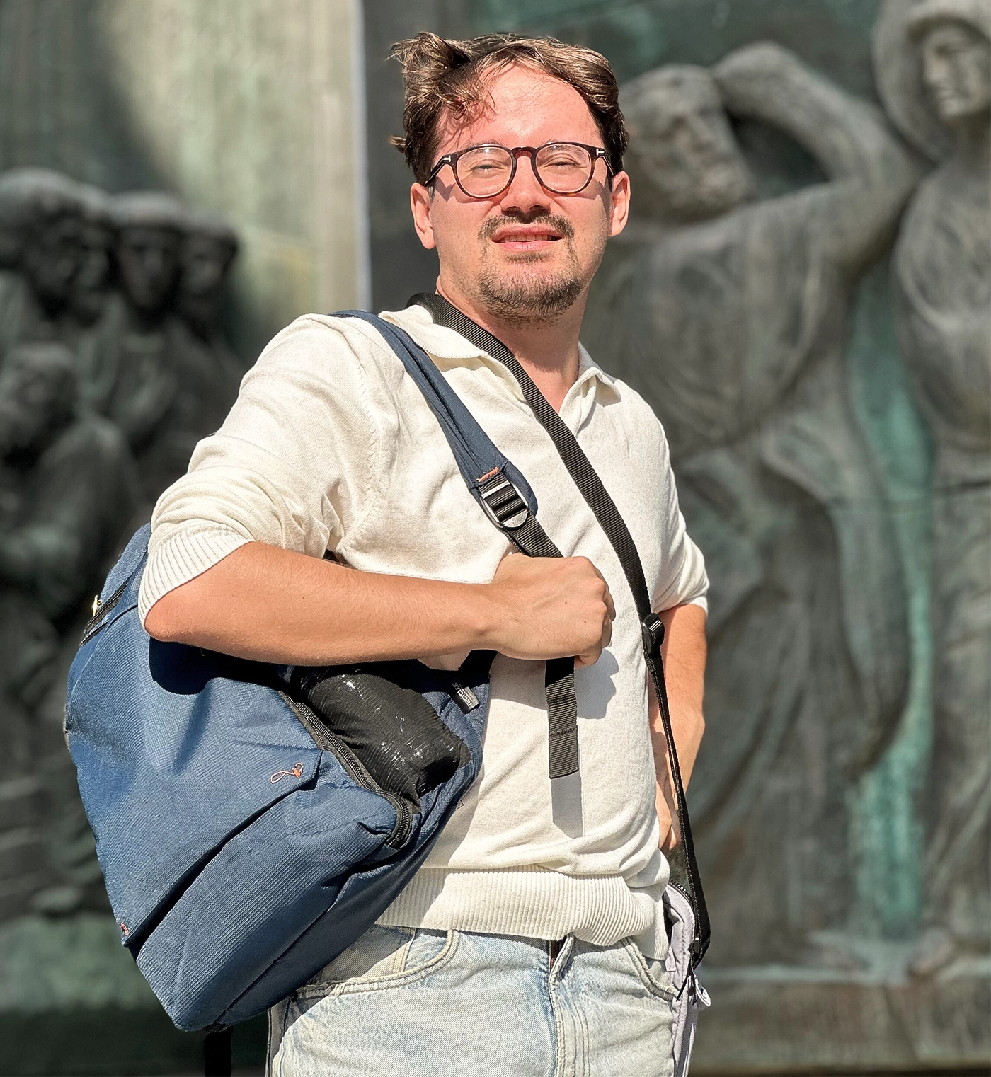 A man with a backpack stands in front of relief carvings outdoors.
