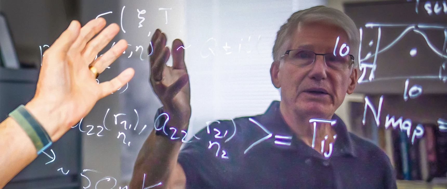A man with white hair and glasses is seen reflected in a shiny blackboard.