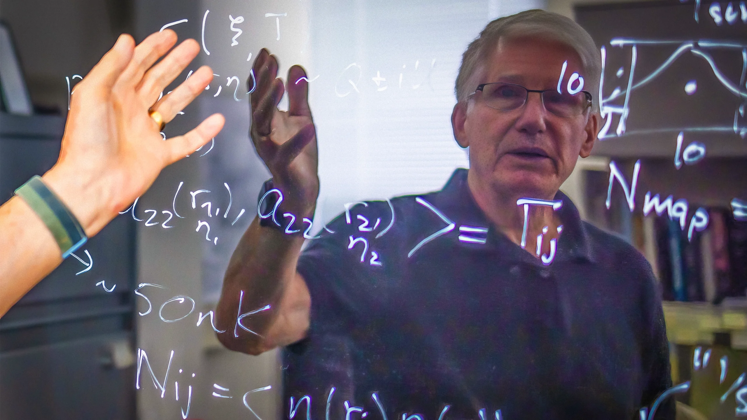 A man with white hair and glasses is seen reflected in a shiny blackboard.