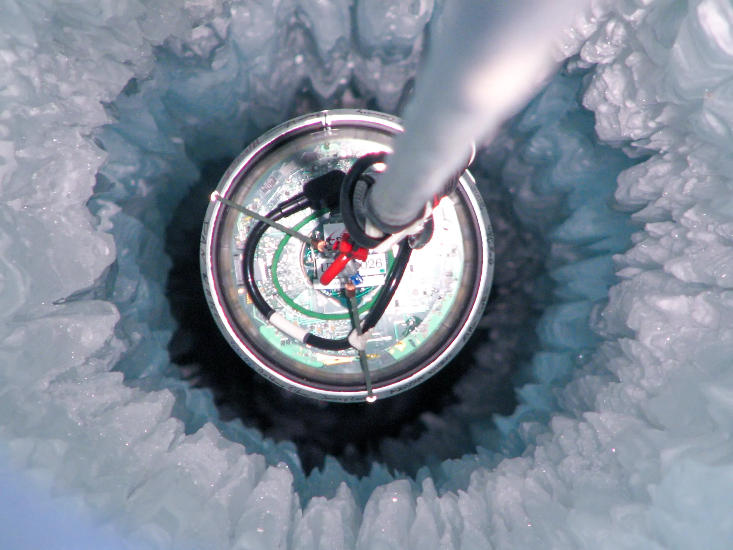 Top-down view of a single spherical detector being lowered through a circular hole drilled into Antarctic ice.